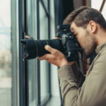 professional male photographer with digital photo camera at window